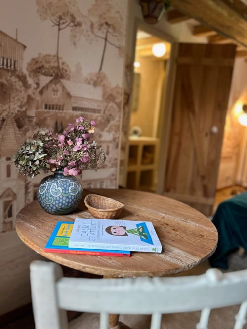 Wooden table at Domaine de Blanvatel with blue vase of pink flowers, books, and basket in cozy interior