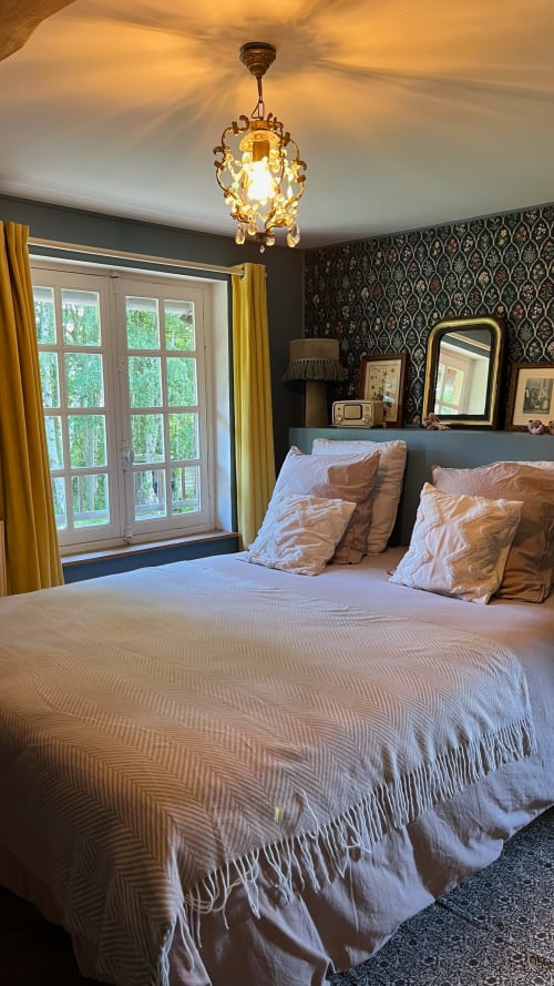 Chambre élégante à la Domaine de Blanvatel avec lustre en cristal, papier peint damassé et vue sur jardin