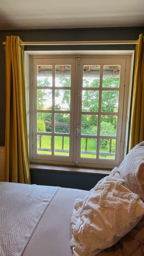 Bedroom at Domaine de Blanvatel with double bed and French doors opening to green gardens in Saint Pierre en Auge