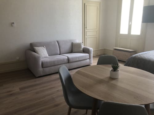 Appartement moderne à Beaune avec canapé gris, table ronde et vue sur la ville près des fenêtres