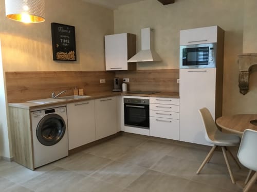 Cuisine moderne de l'appartement Conciergerie Des Climats à Beaune avec armoires blanches, dosseret en bois et électroménagers intégrés
