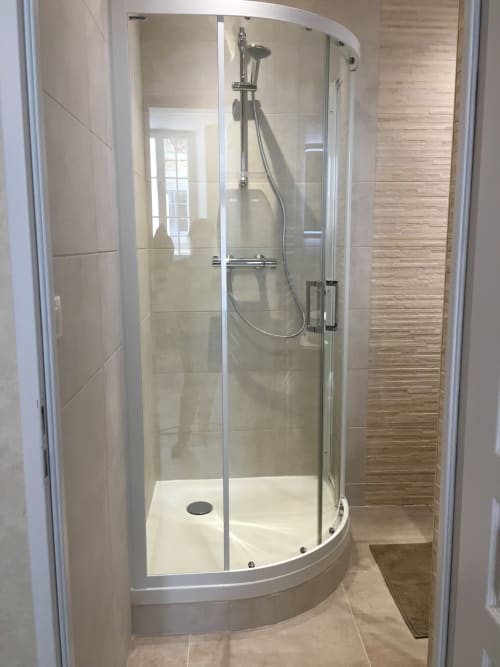 Élégante paroi de douche en verre courbe avec pommeau de pluie et douchette manuelle dans la salle de bain d'un appartement à Beaune.