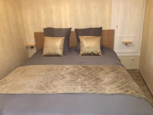 Chambre d'hôtel à Beaune avec lit queen-size, tête de lit grise, coussins dorés et tables de nuit en bois