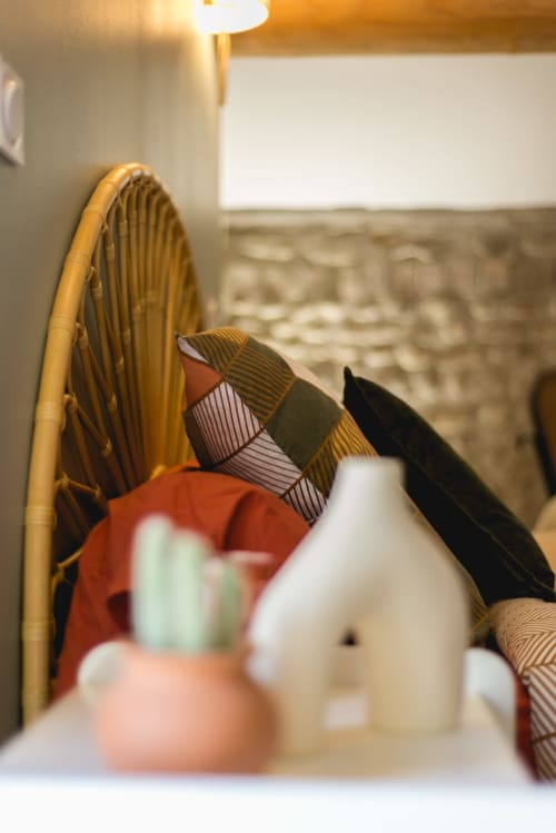Intérieur chaleureux du cottage La Romance avec fauteuil en osier, coussins rayés et vue sur le jardin par la fenêtre