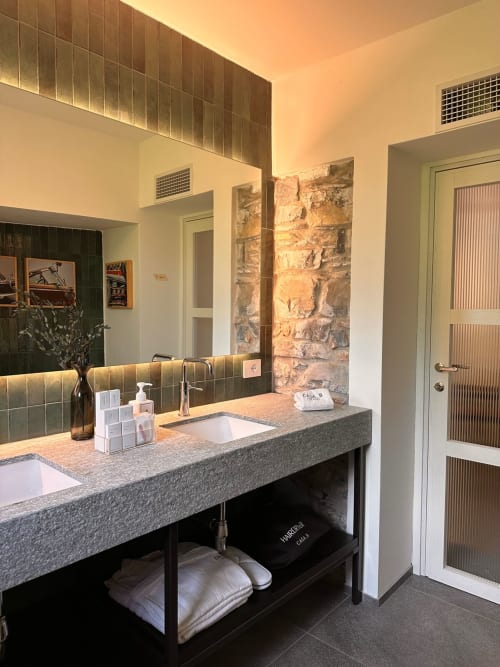 Bagno moderno nell'appartamento Casa_B a Erba con doppi lavandini, parete in pietra naturale e illuminazione calda