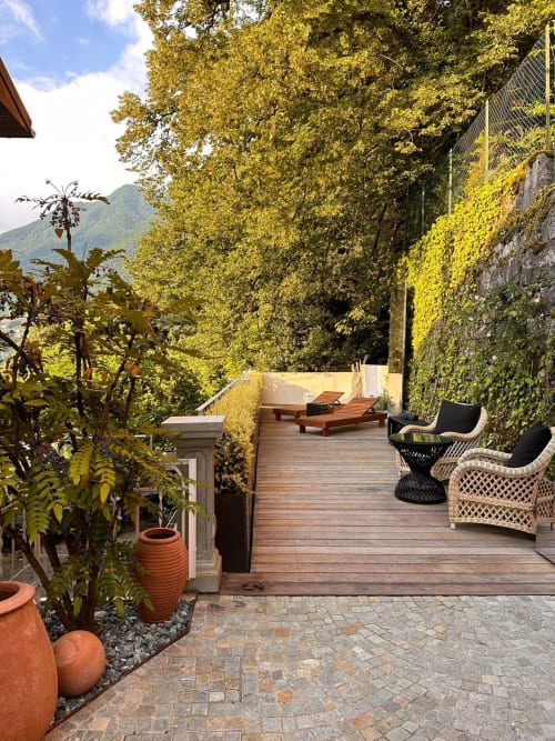 Terrazza ricoperta di edera a Casa_B a Erba con ponte in legno, sedie a sdraio e vista sulle montagne