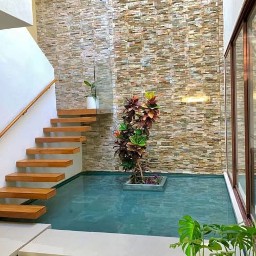 Escalera moderna con escalones de madera y barandilla de vidrio junto a muro de ladrillo texturizado y planta maceta en Alojamientos