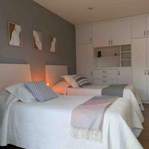 Moderno dormitorio doble en Alojamientos Zoogocho con ropa de cama blanca, pared de acento gris, obras de arte y armarios blancos empotrados