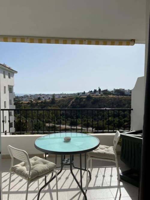 Balcón del apartamento Kandy en Mijas con mesa turquesa, sillas blancas y vistas a la ladera