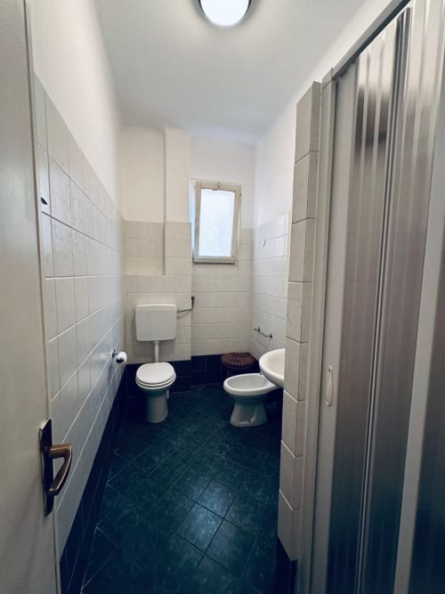 Bagno del B&B Vecchie Mura a Varazze con due toilet, piastrelle beige, pavimento scuro e finestra