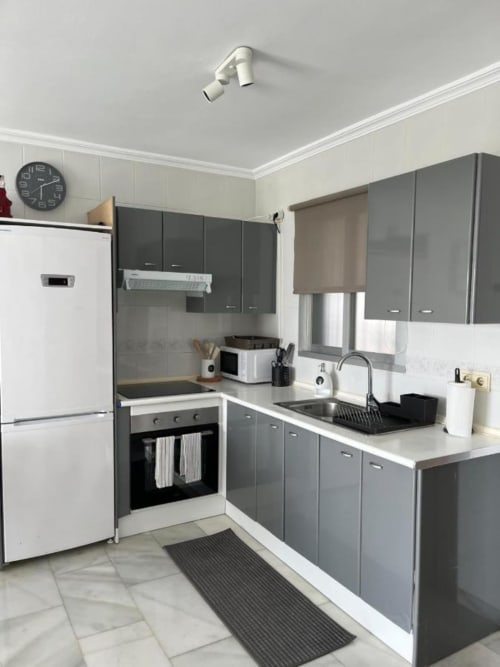 Cocina moderna con muebles grises, encimeras blancas y electrodomésticos de acero inoxidable en Kandy Apartment, Mijas