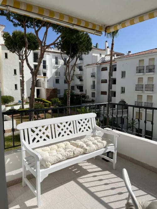 Banco blanco con cojines en balcón soleado con vista a edificios blancos en Mijas