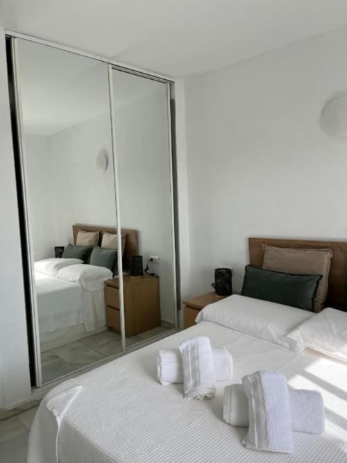 Moderno dormitorio del apartamento Kandy en Mijas con armario espejado, ropa de cama blanca y acceso a vistas al mar