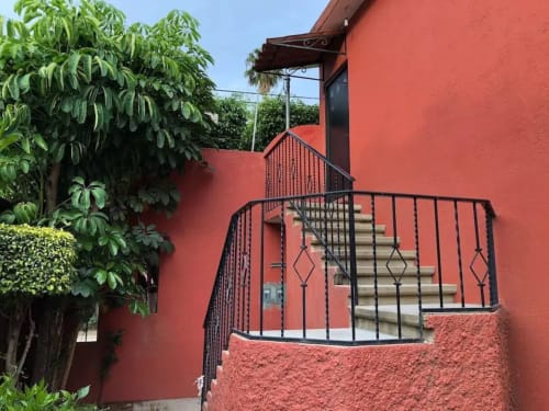 Patio de muros rojos con barandal de hierro negro y escaleras de piedra en Alojamientos Zoogocho, San Andrés Huayapam