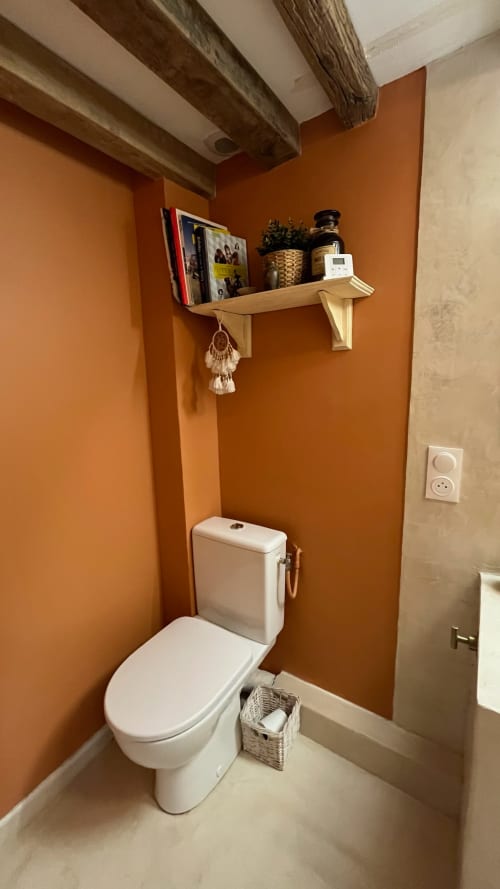 Salle de bain accueillante à la Domaine de Blanvatel avec murs orange, étagère en bois et accessoires blancs