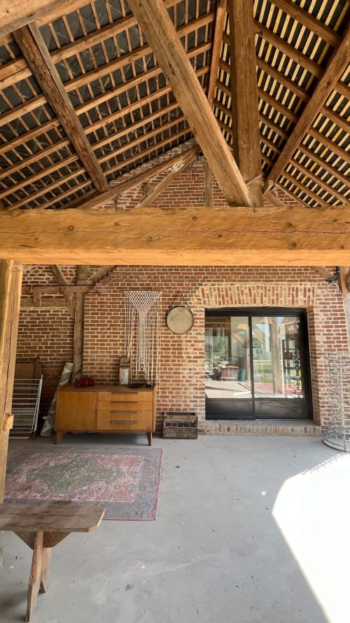 Rustic wooden-beamed interior at Domaine de Blanvatel with exposed brick, vintage furniture, and glass doors