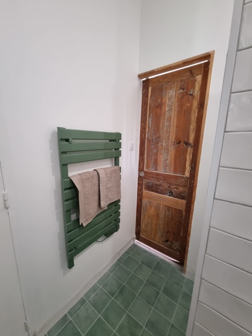 Sèche-serviettes vert et porte en bois dans la salle de bains de Maisonaurinko, Thénon