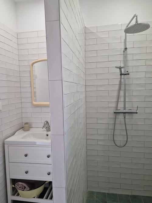 Salle de bains moderne à la Maisonaurinko BnB à Thénon : carrelage blanc métro, douche pluie, lavabo et miroir encadré de bois