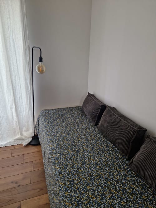 Coin minimaliste de la chambre à la Maison Aurinko B&B à Thénon avec canapé à motifs, lampadaire noir et rideaux blancs