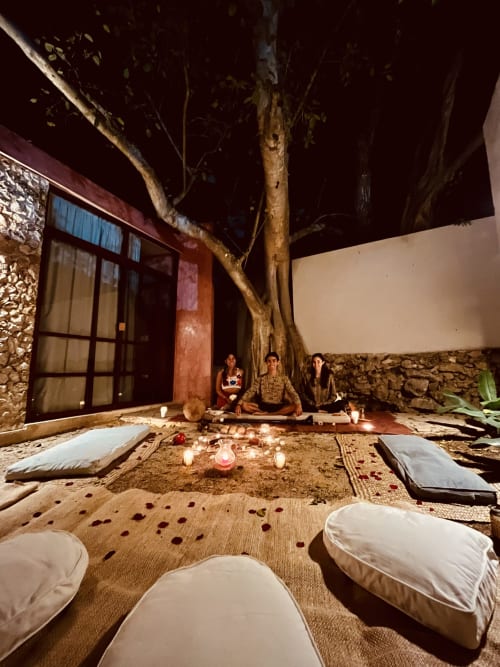 Configuración de ceremonia en el patio de Casa Tuch en Mérida con piso de arena iluminado por velas, cojines y muros de piedra tradicionales bajo cielo estrellado