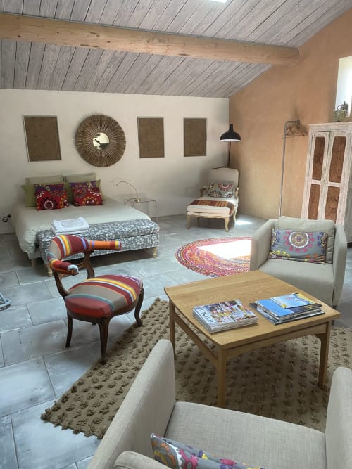 Appartement lumineux et spacieux avec lit, coin salon, table en bois avec magazines, coussins colorés et chaise rayée au Mas du