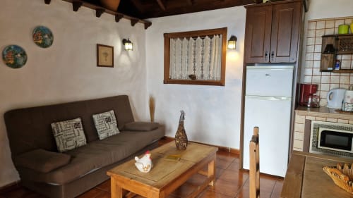 Cozy cottage living room with brown sofa, wooden coffee table, kitchenette, and white refrigerator at Casonas de Marengo in