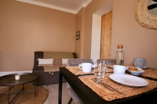 Salle à manger de la villa Tiny Harmony avec table en liège, couverts blancs et murs beige donnant sur le jardin de Venelles