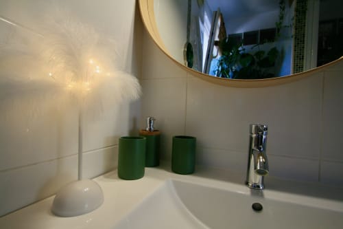 Lavabo moderne de la villa Tiny Harmony avec accessoires verts, miroir rond et décoration en fourrure blanche à Venelles