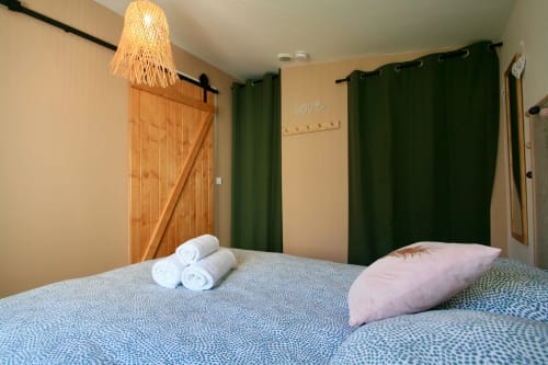 Chambre cosy de la villa Tiny Harmony avec vue sur le jardin, porte de grange en bois, rideaux verts et serviettes roulées sur le lit