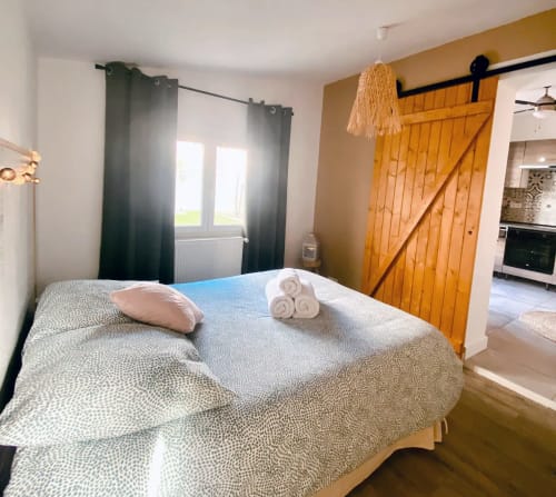 Chambre lumineuse à la villa Tiny Harmony à Venelles avec lit queen-size, rideaux épais, porte grange en bois et vue sur le jardin