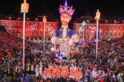 Célébration du carnaval à Nice avec un géant char de roi dominant la foule et les bâtiments illuminés en rouge