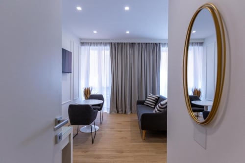 Zona living moderna di CASA LOUNGE ISTRIA a Cagliari con sedie nere, divano, specchio dorato e ampie finestre grigie
