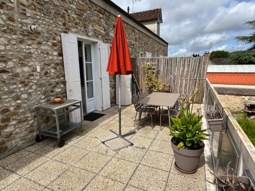 Terrasse de La Barbizonaise avec table à manger, parasol rouge et maison en pierre à Barbizon, France