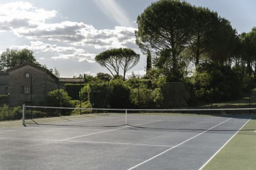 Outdoor tennis court with a net, surrounded by trees and a stone building in the background at Les Terres Aoyama.