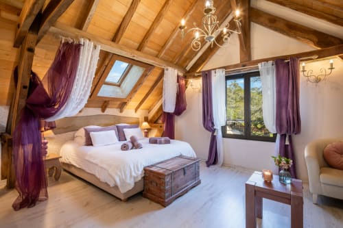 Luxe slaapkamer in Domaine De Campagnac met blootgestelde houten balken, hemelbed met paarse gordijnen en uitzicht op tuin