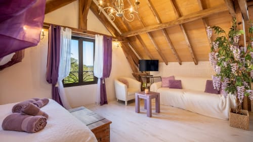 Luxe zolderslaapkamer in Domaine De Campagnac met zichtbare balken, tweepersoonsbedden, paarse accenten en uitzicht op de tuin