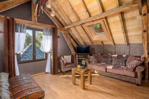 Ruim zolderkamer in Domaine De Campagnac met houten gewelfd plafond, bruine bank, televisie, fauteuil en openslaande deuren