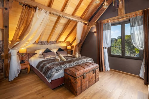 Luxe zolderslaapkamer met hemelbed, houten balken en openslaande deuren met uitzicht op zwembad van Domaine De Campagnac