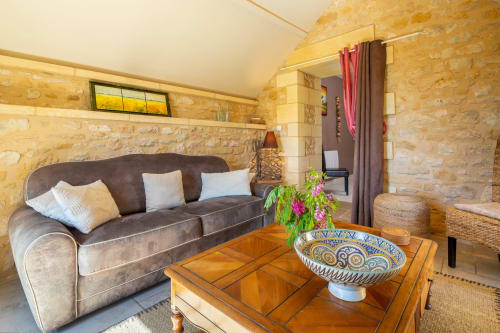 Opaline kamer in Domaine De Campagnac in Carsac-Aillac met bruine bank, houten tafel, stenen muren en uitzicht op het zwembad