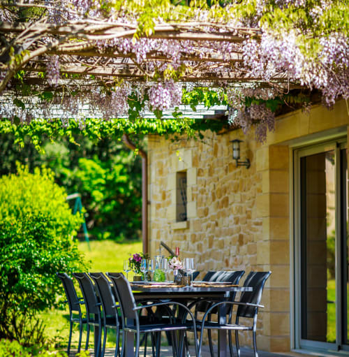 Terrasse fleurie de glycine au Domaine De Campagnac B&B à Carsac-Aillac avec table de repas et maison en pierre