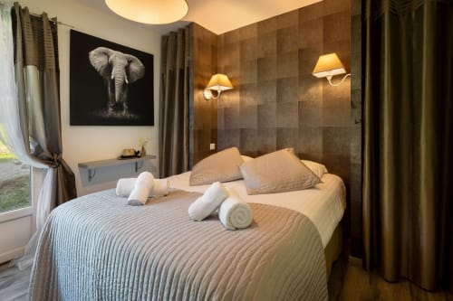 Luxe slaapkamer in cottage Le Catalpa op Domaine De Campagnac met olifantskunstwerk, bruine tegelmuren en uitzicht op de tuin