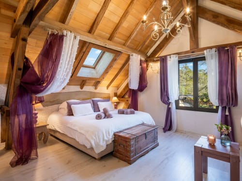 Luxe slaapkamer met houten balken, hemelbedmet paarse gordijnen en zwembadzicht in cottage Domaine De Campagnac