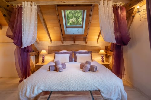 Luxueuze slaapkamer in Carsac-Aillac met lichtkoepel, hemelbed, bordeauxrode gordijnen, houten balken en spa-voorzieningen.