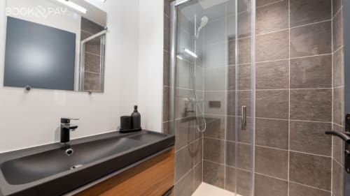 Salle de bain moderne au Domaine de l'Epigny avec lavabo noir, miroir et douche à l'italienne avec carrelage brun