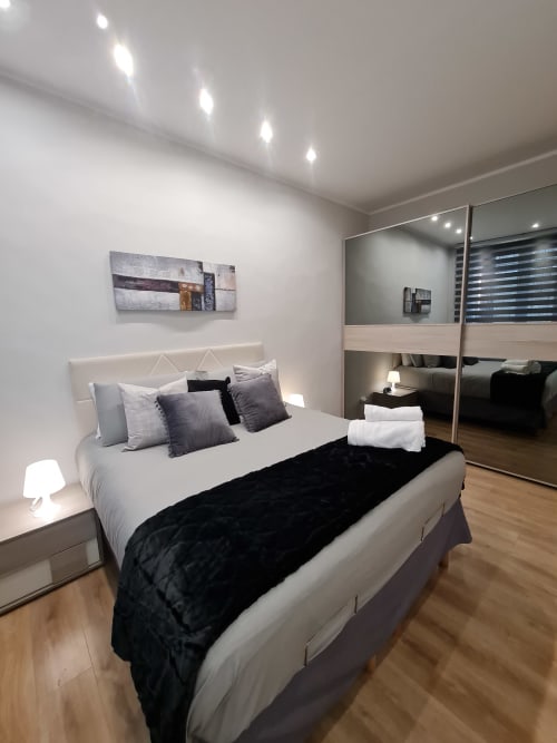 Camera moderna a Raymihome Turin con letto imbottito bianco, armadio a specchio, illuminazione incassata e pavimento in legno