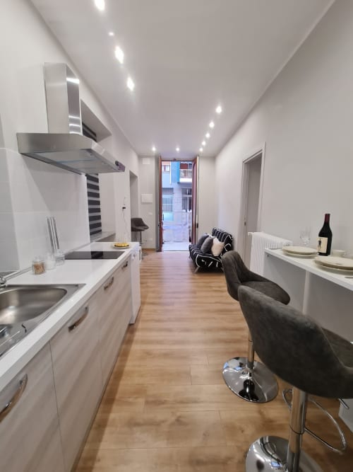 Cucina moderna a pianta aperta e zona living a Raymihome Turin con mobili bianchi, elettrodomestici in acciaio inossidabile e legno