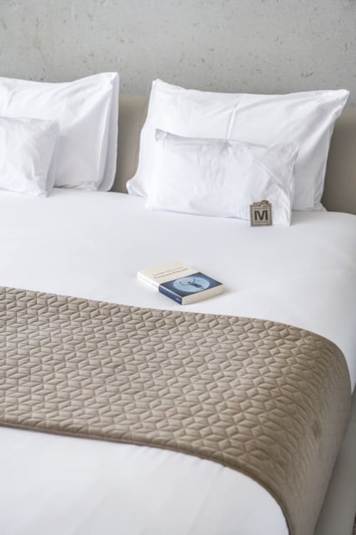 Elegant gestaltetes Bett mit weißen Kissen, beigem Steppwurf und Buch im Boutique-Hotel Le Pavillon M in Grignan