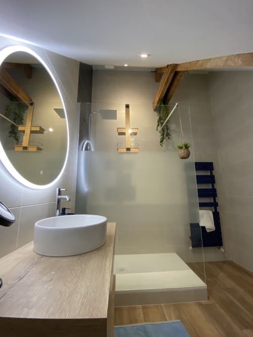Salle de bain spa moderne au gîte Lady Jule avec miroir LED rond, lavabo blanc en vasque, douche ouverte, touches de bois et plantes