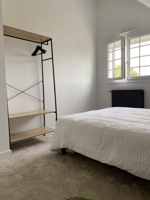 Chambre lumineuse aux Chambres d'hôtes Lady Jule avec lit blanc, portant métallique, étagères et vue sur le jardin