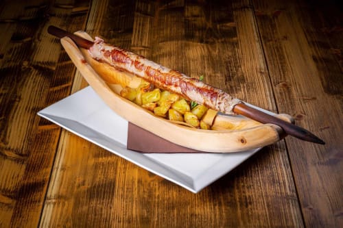 Creative spit-roasted meat and roasted potatoes served in a wooden banana-shaped dish at Al Dos, Livigno